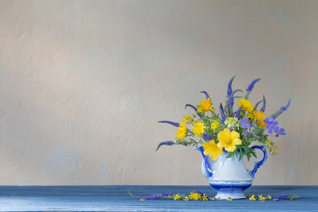Ramo con flores azules y amarillas en tetera sobre mesa de madera