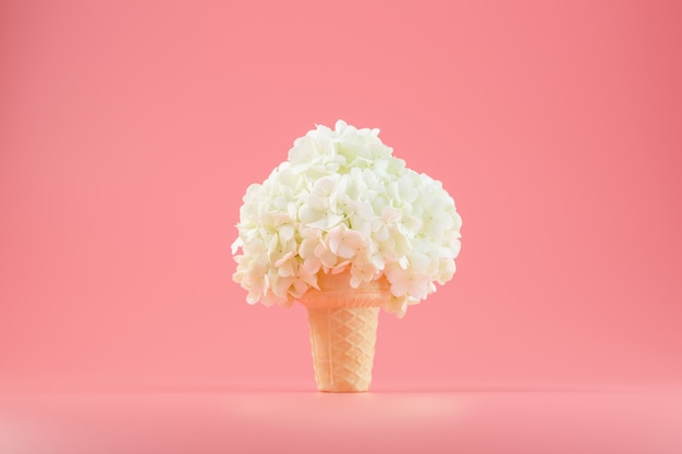 Un ramo de flores blancas en un cono de helado en rosa.