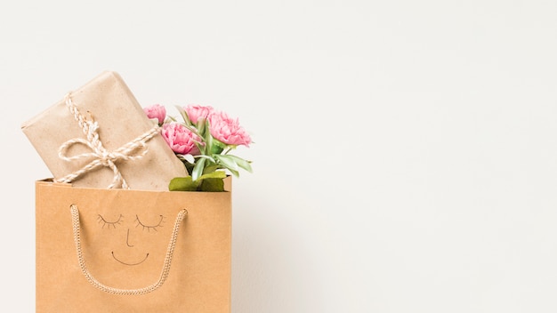 Ramo de flores y caja de regalo envuelta en una bolsa de papel con cara dibujada a mano aislada sobre fondo blanco