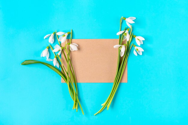 Ramo de flores de campanillas y papel artesanal para notas sobre fondo azul Vista plana endecha superior