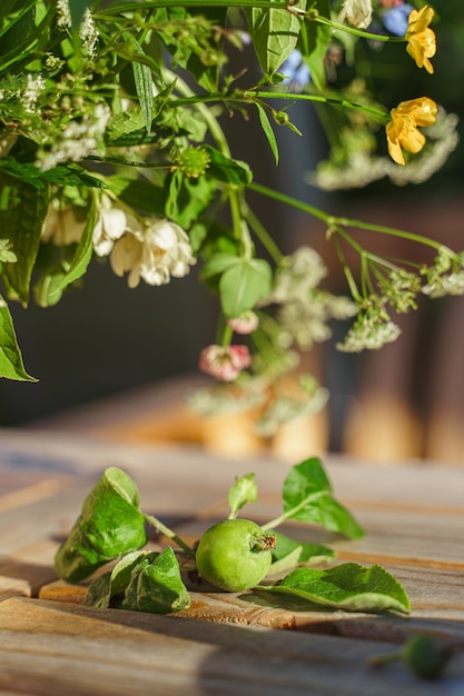 Foto ramo de flores de campo y una manzana verde inmadura sobre una mesa de jardín iluminada por los rayos del sol poniente