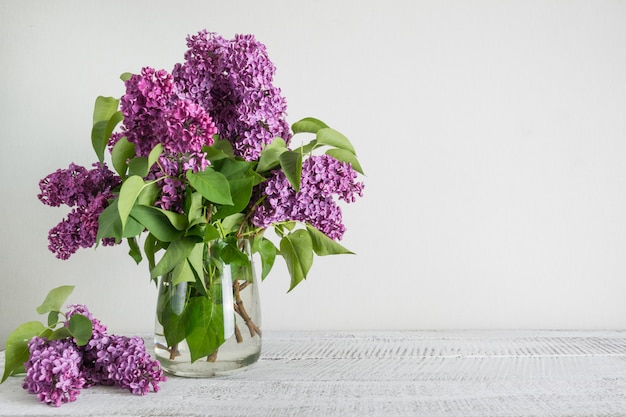 Ramo de flores de color lila púrpura en florero de cristal en el interior blanco. Espacio para texto.
