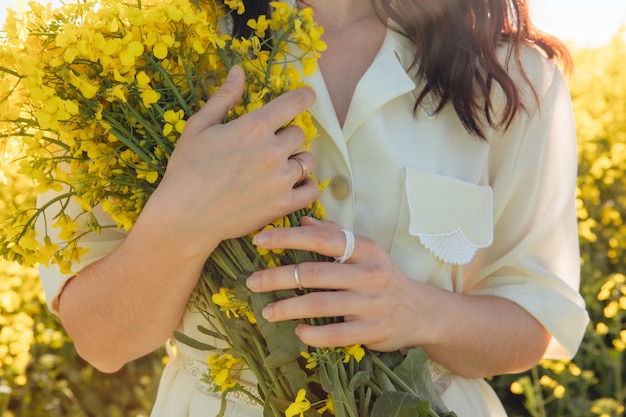 Ramo de flores de colza en manos de mujer sin rostro de cerca