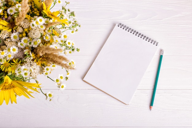 Ramo de flores, cuaderno y lápiz sobre una mesa blanca.