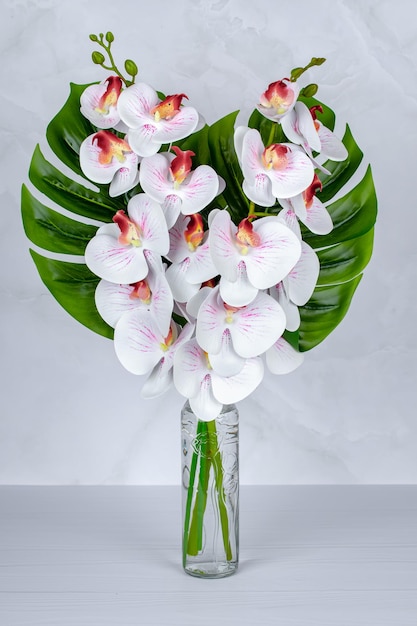 Un ramo de flores en un jarrón de orquídeas blancas en una botella de vidrio sobre una mesa gris Decoración interior del hogar F ...