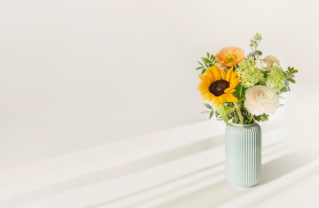 Ramo con flores en un jarrón sobre la mesa con el fondo de una pared blanca.