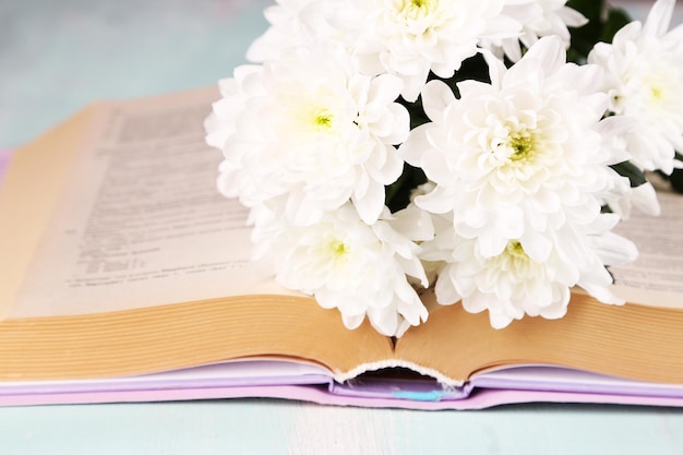 Ramo de flores con libro sobre mesa de madera de color closeup