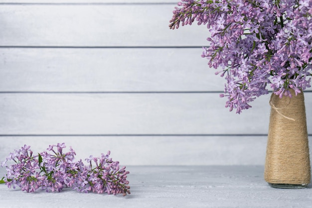 Ramo de flores lilas en jarrón y rama sobre mesa sobre fondo gris de madera Copiar espacio