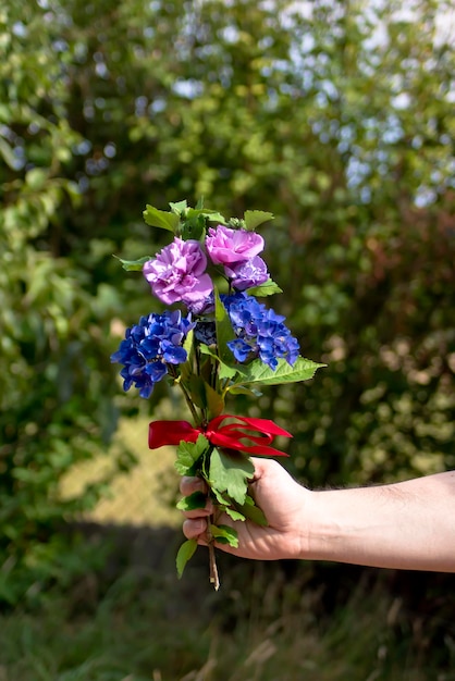 Un ramo de flores en una mano con una cinta roja atada alrededor