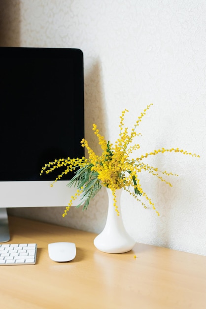 Ramo de flores de mimosa amarillas en un jarrón en un escritorio con una computadora