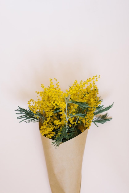 Ramo de flores de mimosa en una bolsa artesanal sobre un fondo blanco con un espacio para copiar