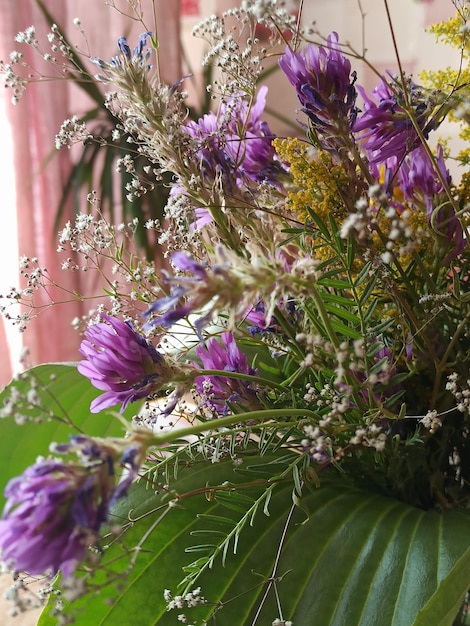 Un ramo de flores moradas está en un jarrón con una hoja verde.