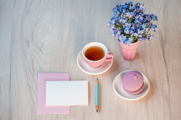 Un ramo de flores no me olvides en una mesa con una taza de té y una tarjeta para el texto de felicitación.