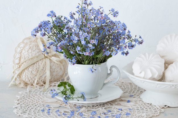 Un ramo de flores nomeolvides en una mesa en una taza blanca, un corazón hecho de encaje