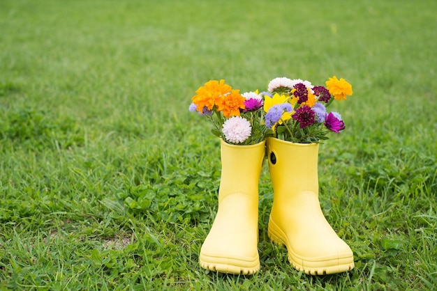 Un ramo de flores de otoño en botas amarillas sobre un fondo de hierba verde