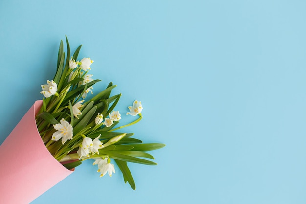 Ramo de flores de primavera en cono de papel rosa sobre fondo azul endecha plana Feliz día de la madre