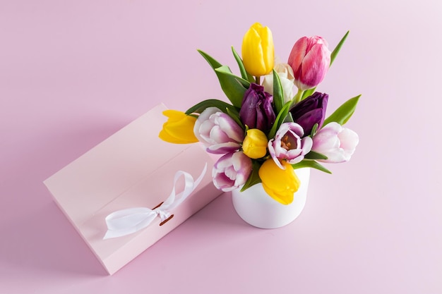 Un ramo de flores de primavera en un jarrón blanco junto a una caja de regalo con un fondo rosa de cinta el concepto de regalo y buen humor