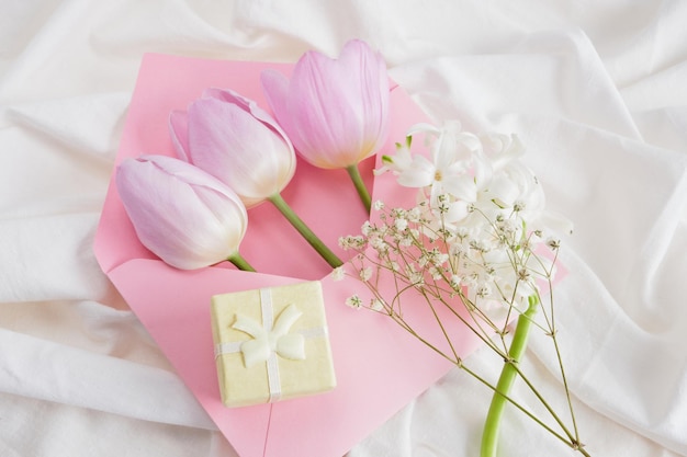 Un ramo de flores de primavera en tonos delicados una pequeña caja de regalo amarilla y un sobre rosa en la cama un regalo romántico para un amante 8 de marzo o 14 de febrero