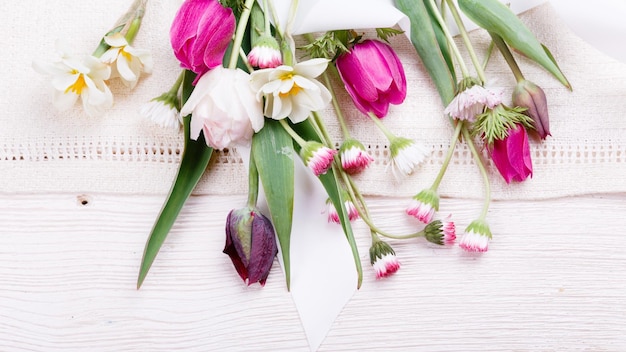 Ramo de flores de primera primavera, tulipanes de color rosa púrpura, narcisos y margaritas sobre fondo de madera blanca, vista superior, endecha plana, Pascua, cumpleaños, madre, San Valentín, día de la boda de la mujer, concepto