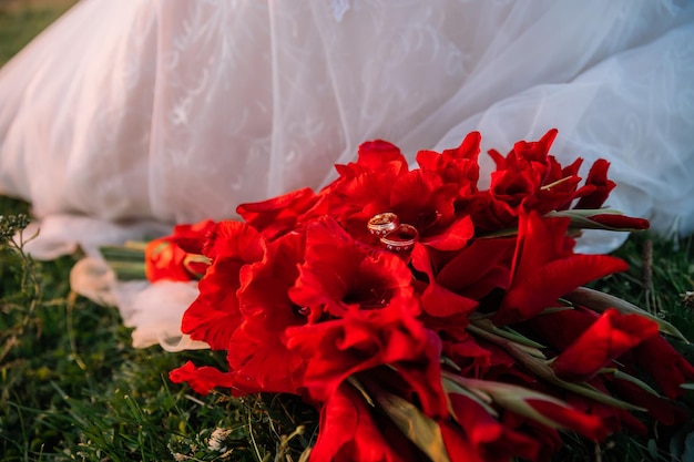 Ramo de flores rojas se encuentran en la hierba verde cerca de la novia vestido blanco