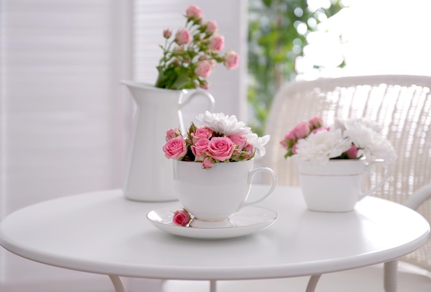 Ramo de flores de rosa y crisantemo en taza sobre mesa