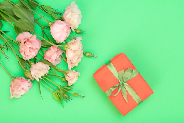 Ramo de flores rosas con hojas y caja de regalo con cinta sobre fondo verde. Vista superior. Concepto de día de celebración.