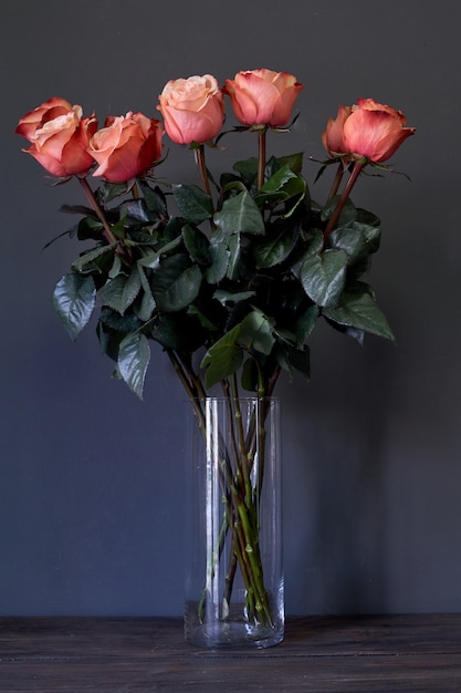 Ramo de flores rosas en un jarrón de cristal alto y claro contra una pared gris, enfoque selectivo