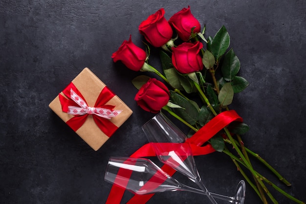 Ramo de flores rosas rojas, caja de regalo, copas de champán sobre fondo de piedra negro Tarjeta de felicitación del día de San Valentín