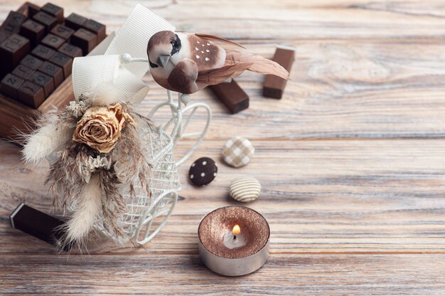 Ramo de flores secas en bicicleta decorativa con pequeño pájaro marrón y vela encendida sobre la mesa. Tarjeta de felicitación para boda o vacaciones en tonos naturales.