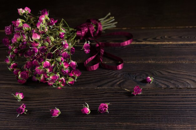 Ramo de flores secas con una cinta sobre la superficie de madera oscura.