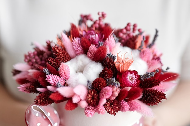 Ramo de flores secas con pastos en caja de sombrero redonda rosa en las manos