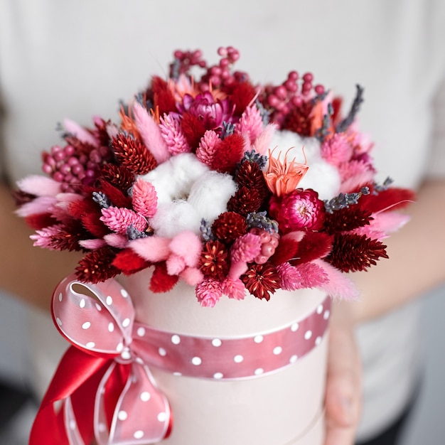 Ramo de flores secas con pastos en caja de sombrero redonda rosa en las manos