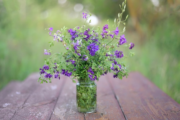 Ramo de flores silvestres en azul y morado en un frasco de vidrio sobre una mesa de madera vintage