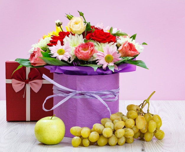 Ramo de flores silvestres, caja de regalo, uvas y una manzana en las tablas de madera