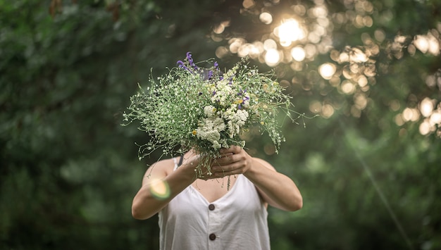 Un ramo de flores silvestres en manos de una niña sobre un fondo borroso en el bosque.