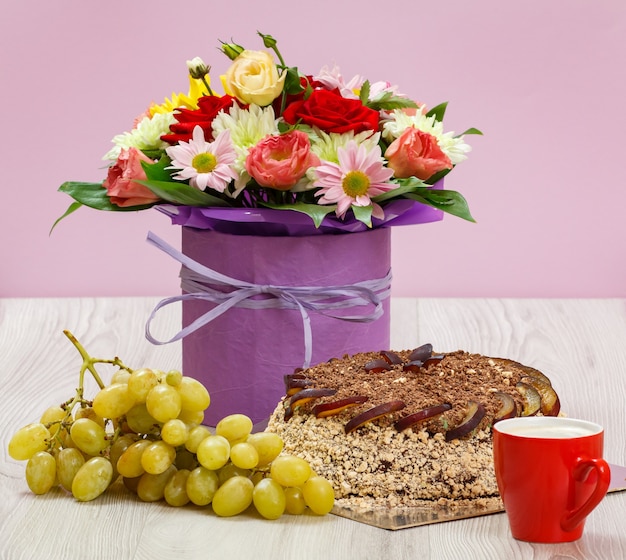 Ramo de flores silvestres, un pastel de chocolate, uvas y una taza de café en las tablas de madera.