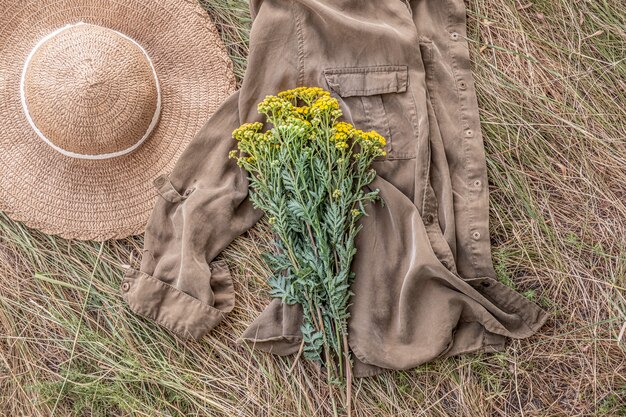 Un ramo de flores silvestres sobre el césped desvaído y el sombrero del país. Bodegón rural en posición horizontal: el ramo descansa sobre una camisa en la hierba o el heno.