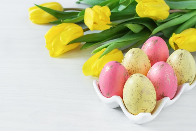 Ramo de flores de tulipán amarillo primaveral y coloridos huevos de Pascua sobre fondo blanco de madera