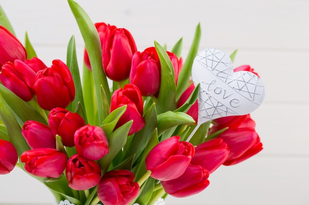 Ramo de flores de tulipán rojo fresco en el estante delante de la pared de madera.