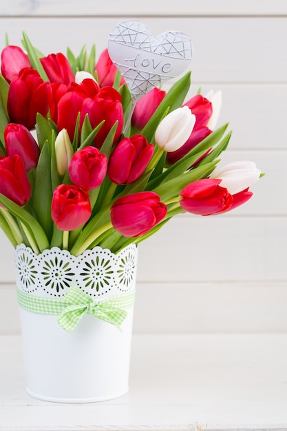 Ramo de flores de tulipán rojo fresco en el estante delante de la pared de madera.