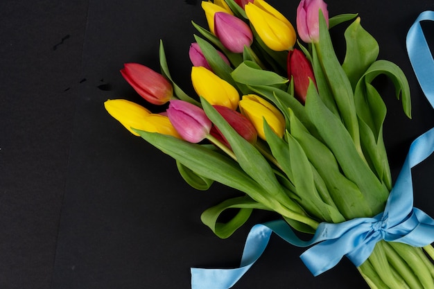 Ramo de flores de tulipanes rosa, rojo y violeta con corazones sobre fondo negro