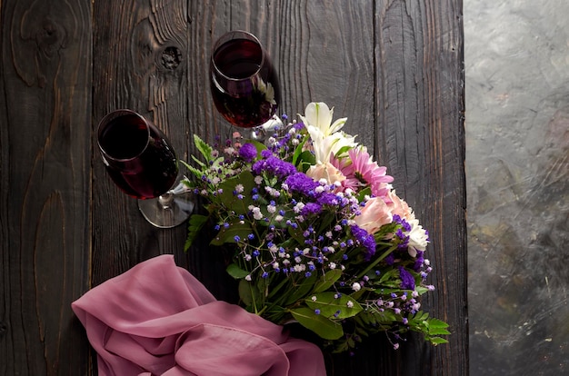 Un ramo de flores variadas, suaves y festivas y dos copas de vino en una mesa de madera