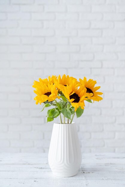 Un ramo de girasoles en un jarrón contra el fondo de una pared de ladrillo blanco Copiar espacio para texto