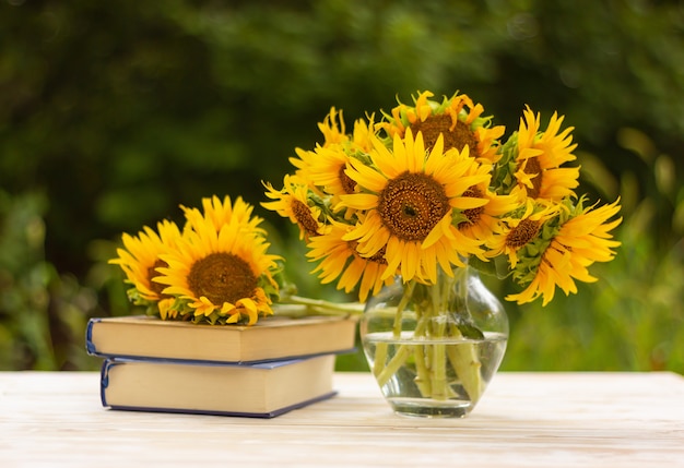 Ramo de girasoles en un jarrón y una pila de libros sobre una mesa en el jardín