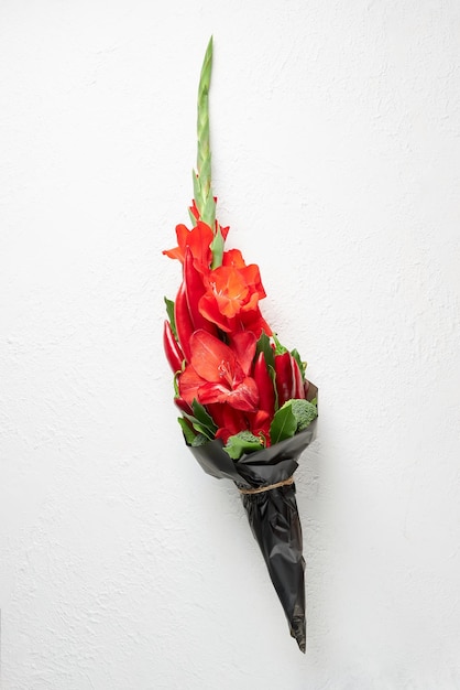 Foto ramo de gladiolos rojos pimiento rojo decorado con hojas de laurel y brócoli sobre un fondo blanco.