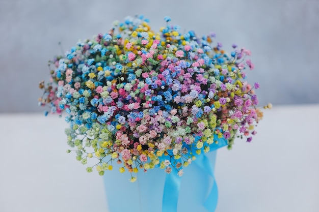 Ramo de gypsophila multicolor en una caja azul con un lazo sobre un fondo gris