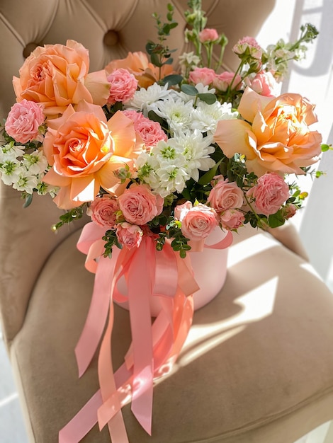 Un ramo de hermosas flores de durazno en una caja se encuentra en una silla en una florería. Una composición de rosas, mattiola blanco y crisantemo. Un dulce regalo para unas vacaciones.