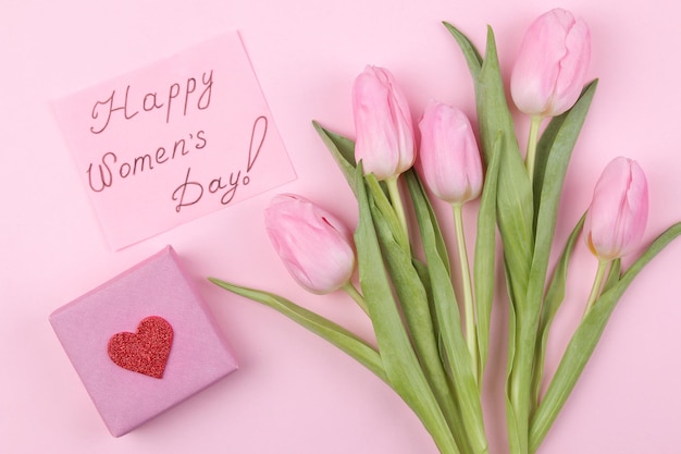 Un ramo de hermosas flores de tulipanes rosas y una caja de regalo sobre un fondo rosa de moda Vacaciones de primavera texto feliz día de la mujer vista superior
