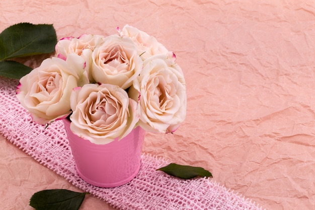 Un ramo de hermosas rosas se encuentra en un pequeño cubo en una cinta de encaje sobre un fondo rosa artesanal