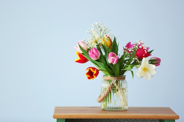 Ramo de hermosos tulipanes de colores en la mesa de madera contra la pared azul claro